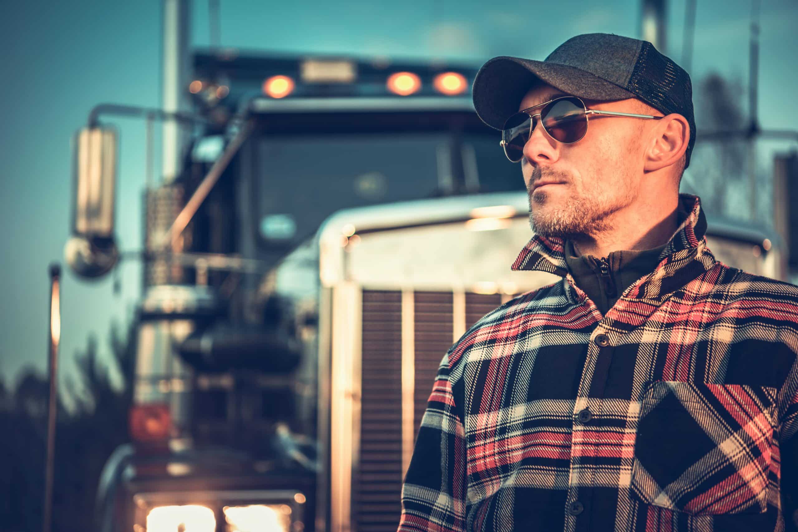 Semi-truck driver wearing sunglasses, standing in front of truck
