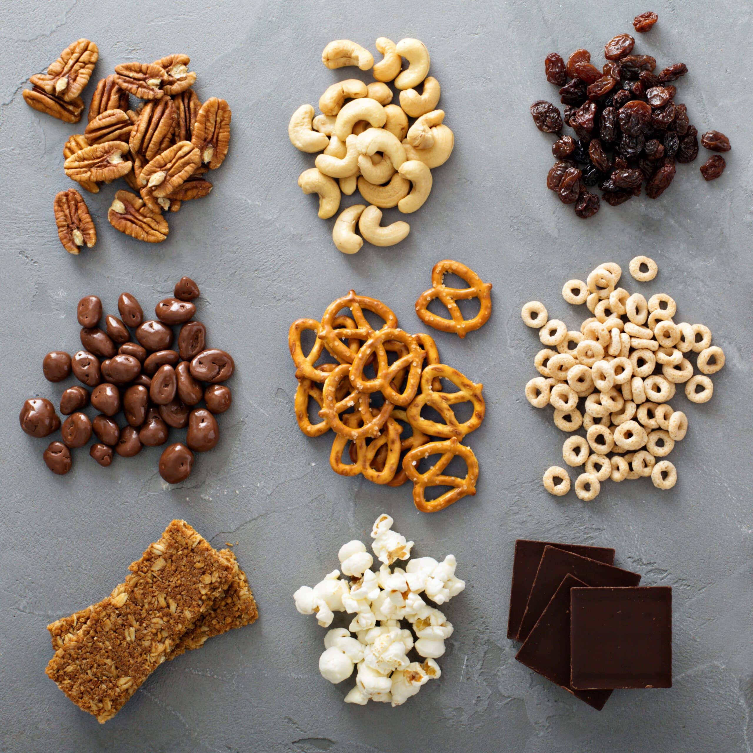 Small piles of healthy snacks like nuts, raisins, pretzels, popcorn, dark chocolate